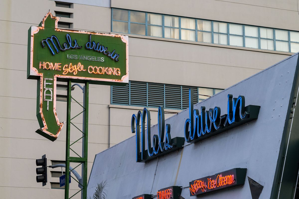 A green sign with arrow points to a Googie diner at daytime.
