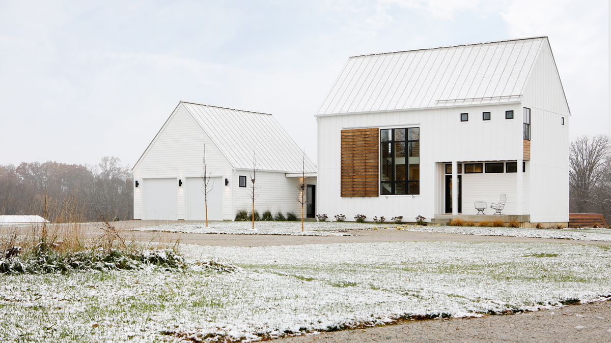 The exterior of two buildings. Both buildings are painted white. In the foreground is a lawn covered in frost and snow. 