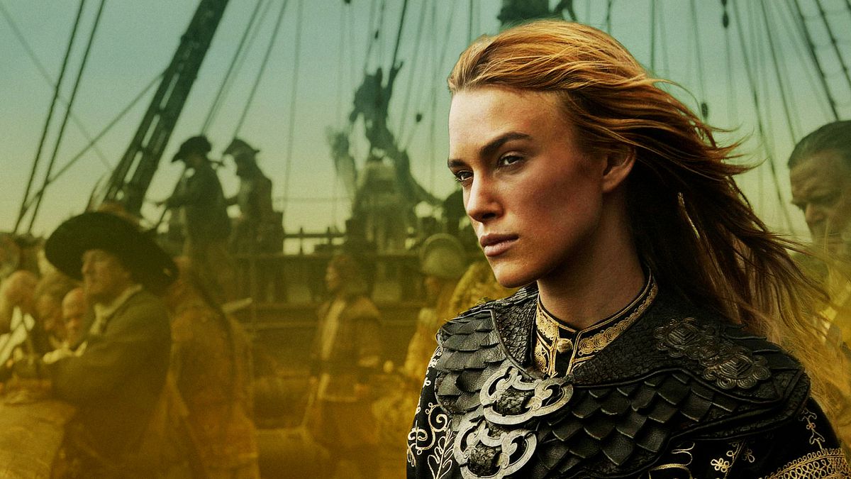 elizbeth swann in her pirate king coat. her blonde hair blows in the sea wind and she looks determined and fierce. behind her is a ship, the background blurred to emphasize her