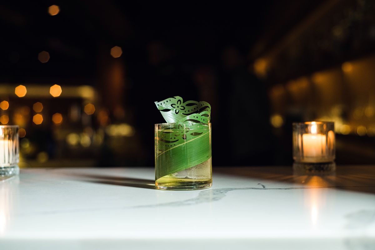A glass with a green leaf garnish sits on a white marble countertop.