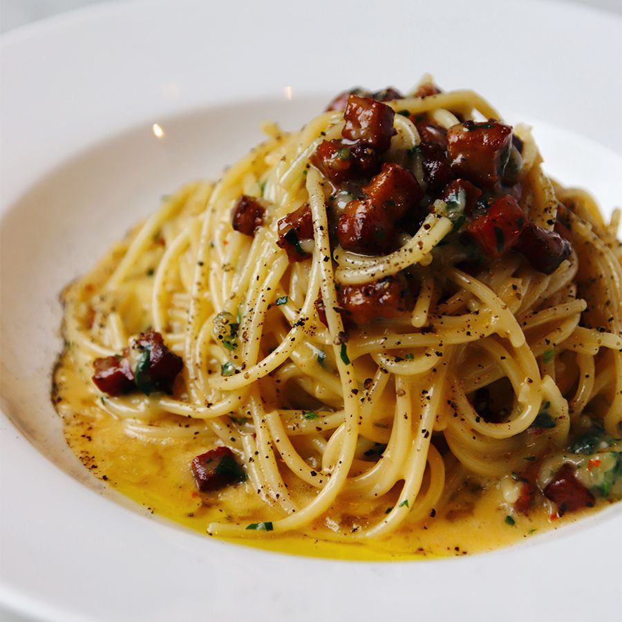 A plate of spaghetti carbonara piled in a white dish. 