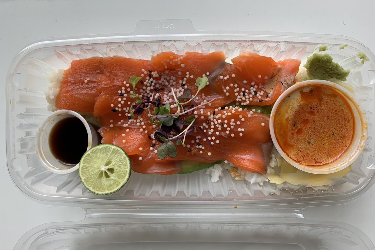 A plastic container with slices of salmon, and a large condiment saucer of orange sauce and two smaller ones one with dark soy sauce and the other with a green sauce.