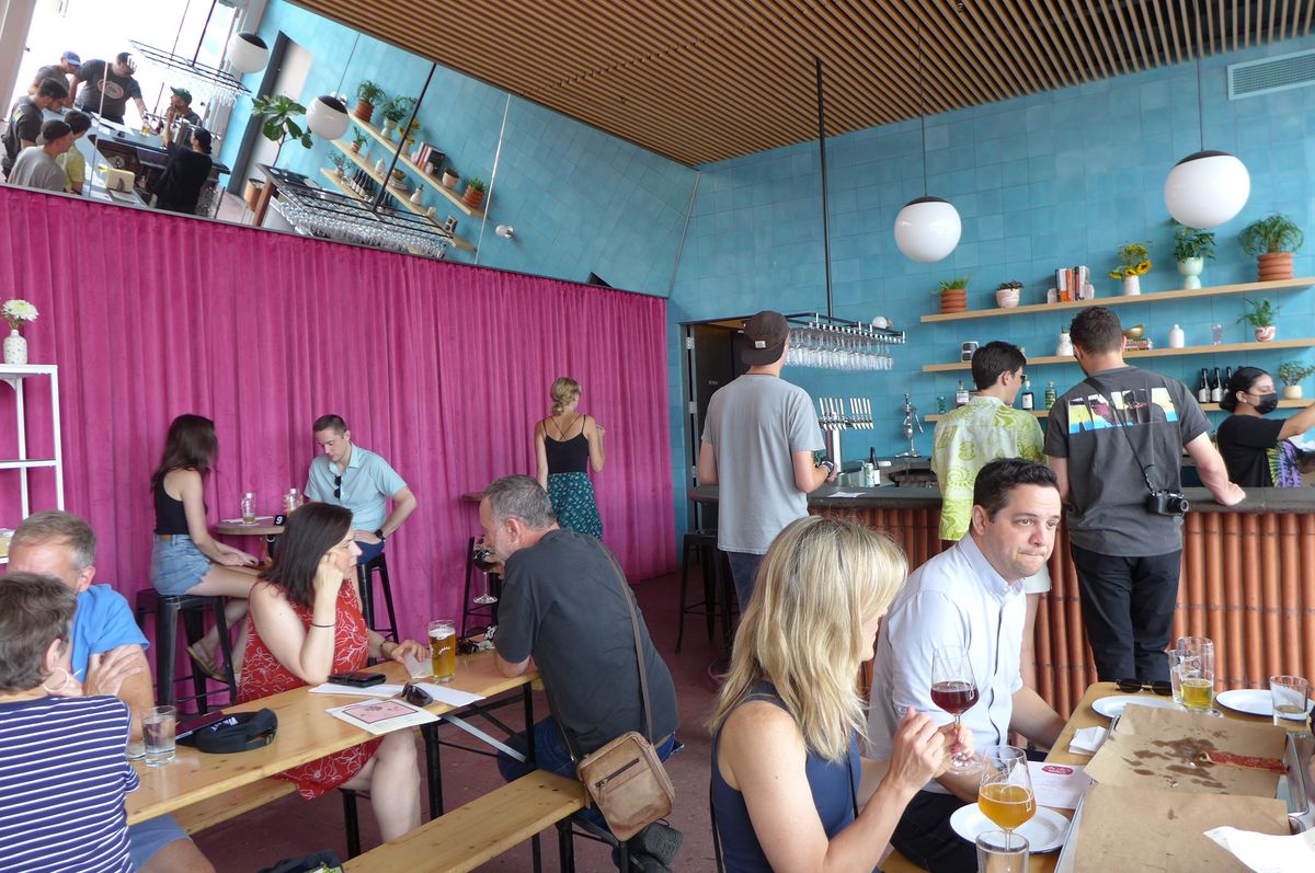 People sit at tables drinking beer and wine with colorful walls in red and dark green behind them.