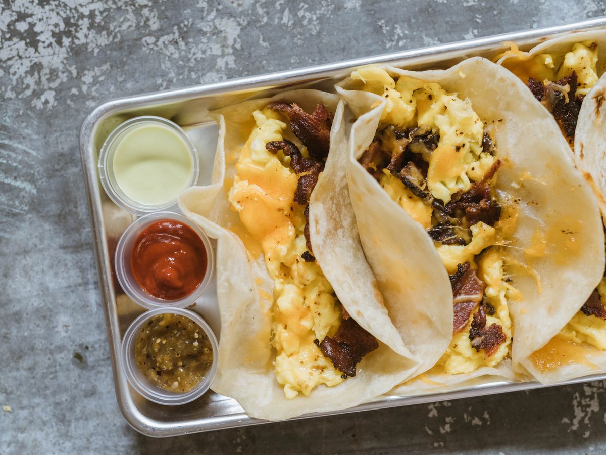 a tray holds three salsas and 3 breakfast tacos filled with egg and meat and cheese