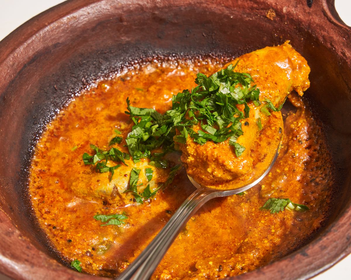 A close up of red and orange sauce and food in a red clay bowl, garnished with shredded green herbs.