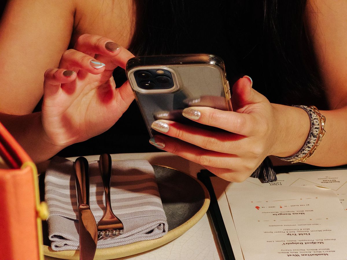 A closely cropped photo of a woman sitting at a table and scrolling through her phone.