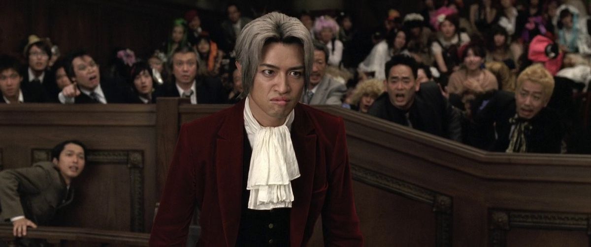 The crowd in the live action adaptation of Ace Attorney responds by leaning in during a crucial moment, behind the scowling face of Miles Edgworth.