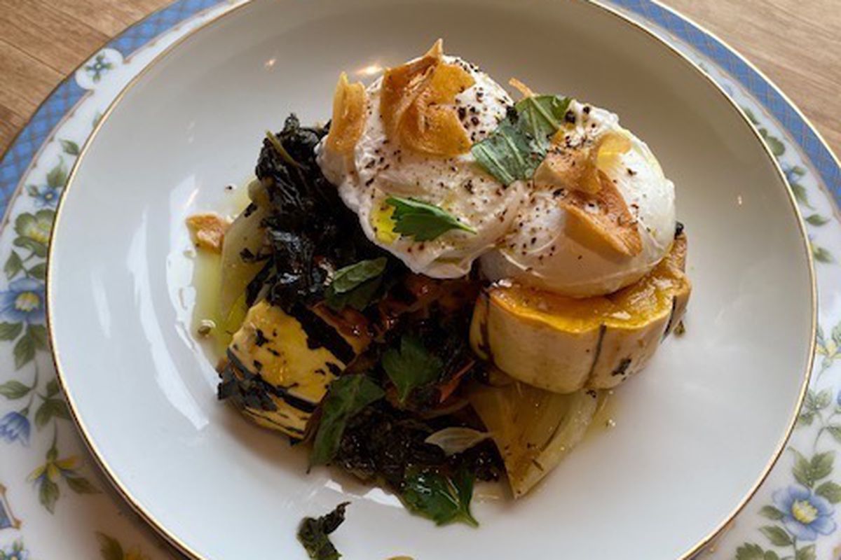 A close up of a poached egg dish, on top of squash, kale, and tomatoes.