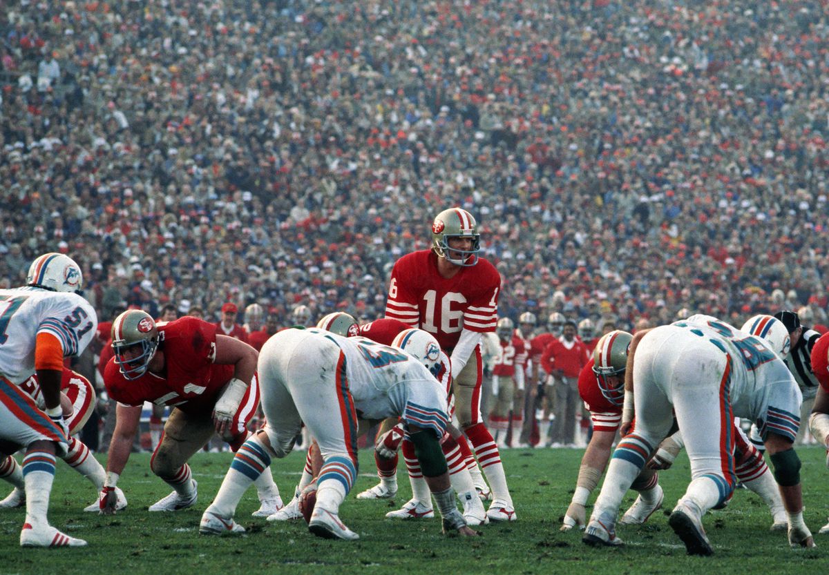 Quarterback Joe Montana of the San Francisco 49ers stands behind center Fred Quillan as offensive lineman Randy Cross looks on and as linebacker Mark Brownand defensive linemen Bob Baumhower and Kim Bokampe of the Miami Dolphins are set to pursue the play during Super Bowl XIX at Stanford Stadium on January 20, 1985 in Stanford, California. The 49ers defeated the Dolphins 38-16.