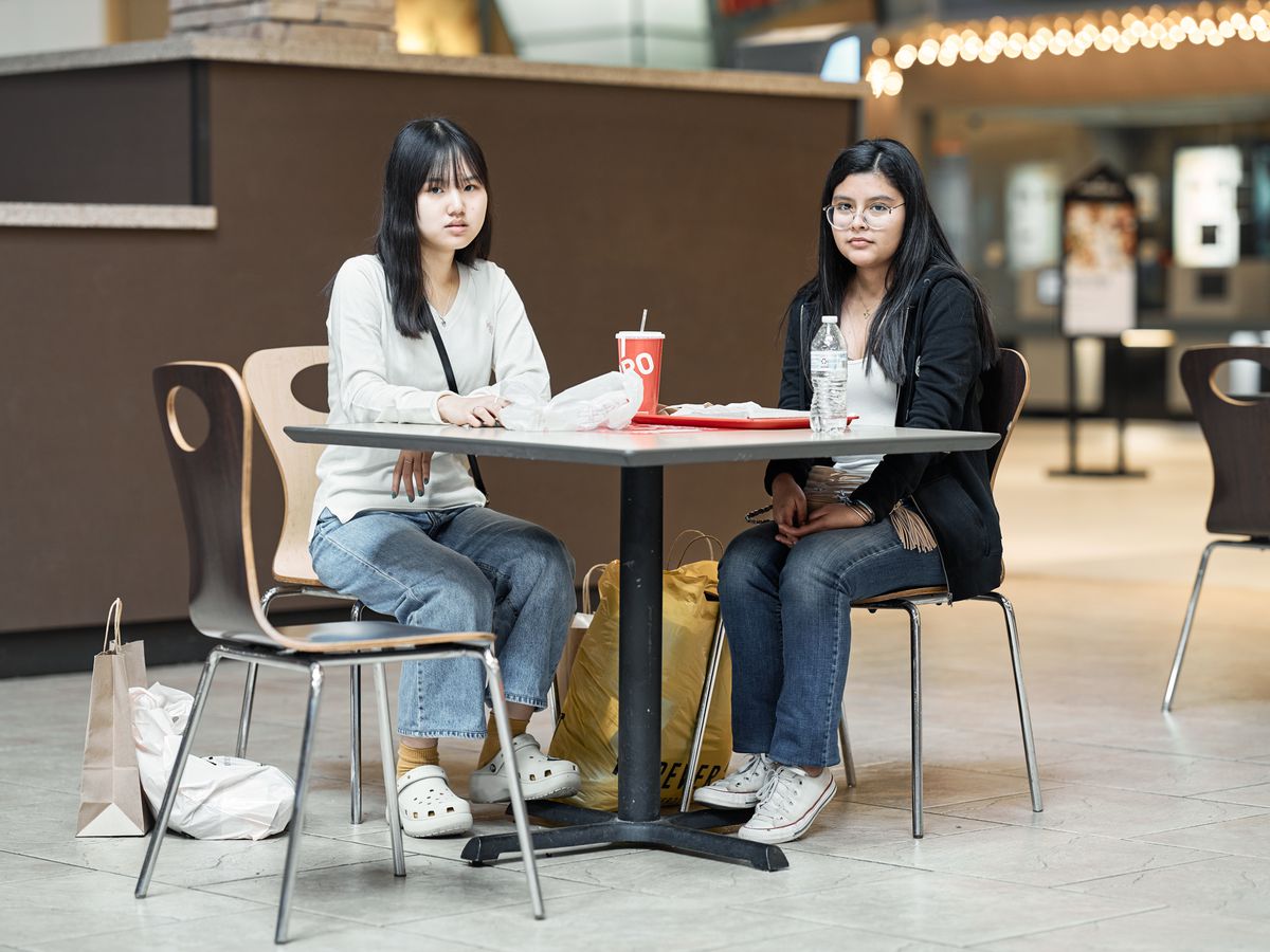 Two teen girls sitting at a food court table.