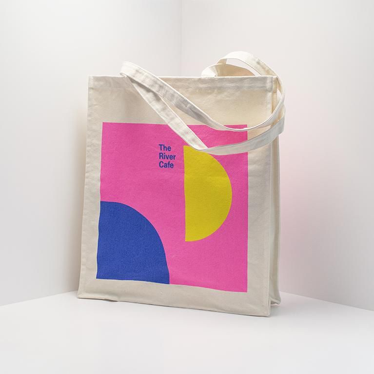 A River Cafe-branded tote bag with pink, blue, and yellow geometric patterning