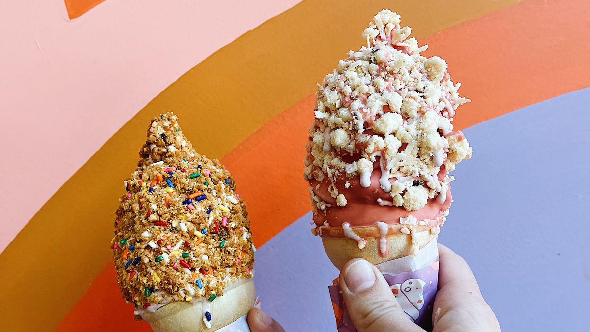 Two hands, one brown skinned and one light skinned, holding soft serve cones dipped in hard chocolate shells, coated in sprinkles.