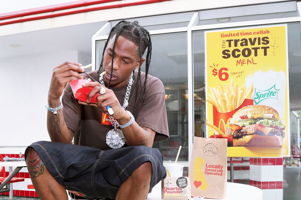 Travis Scott sitting on a table outside McDonald’s, advertising his new $6 meal.