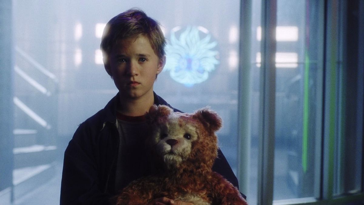David (Haley Joel Osment) holds a teddy bear in front of glowing neon signs in A.I. Artificial Intelligence 