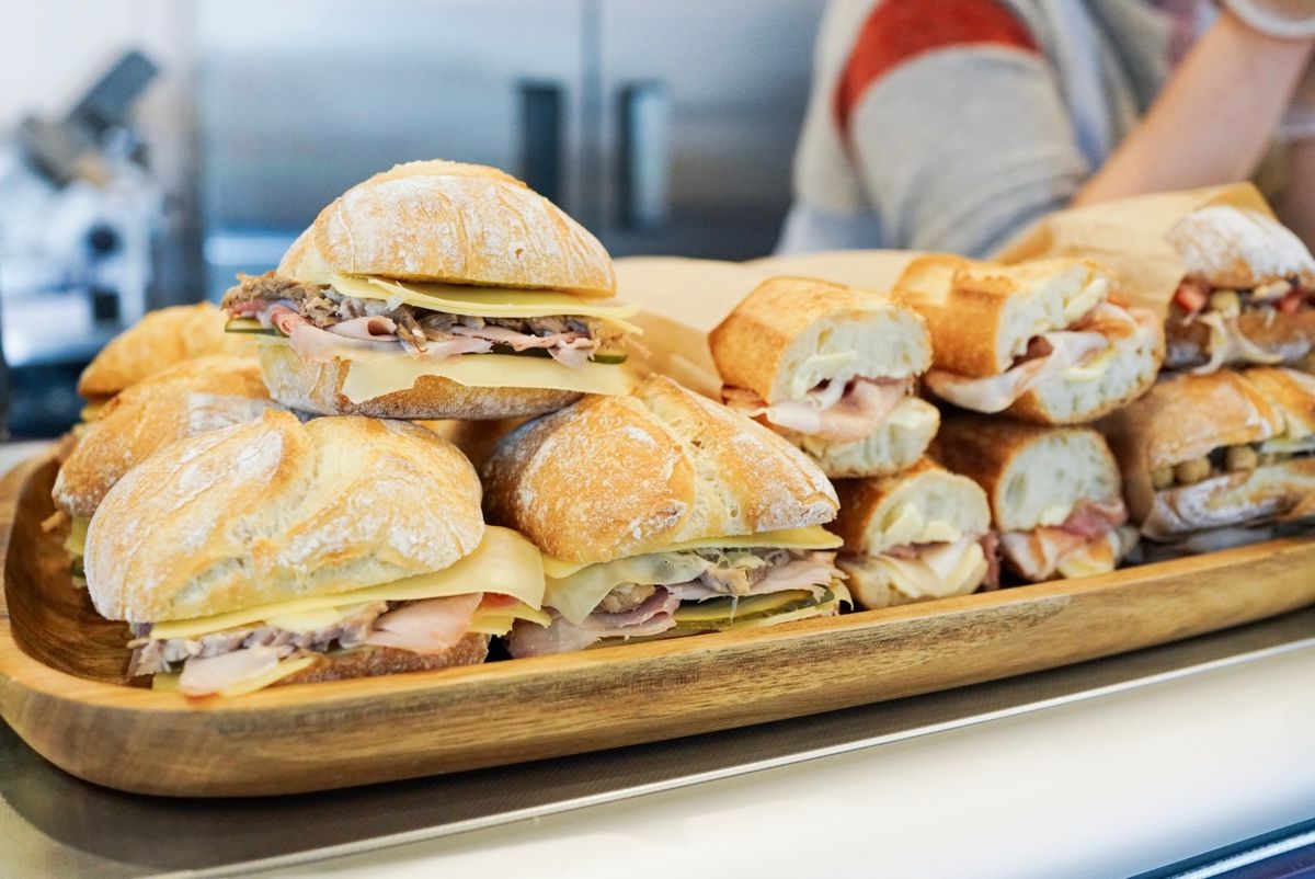 A row of sandwiches on a wooden board sit on top of a deli counter case