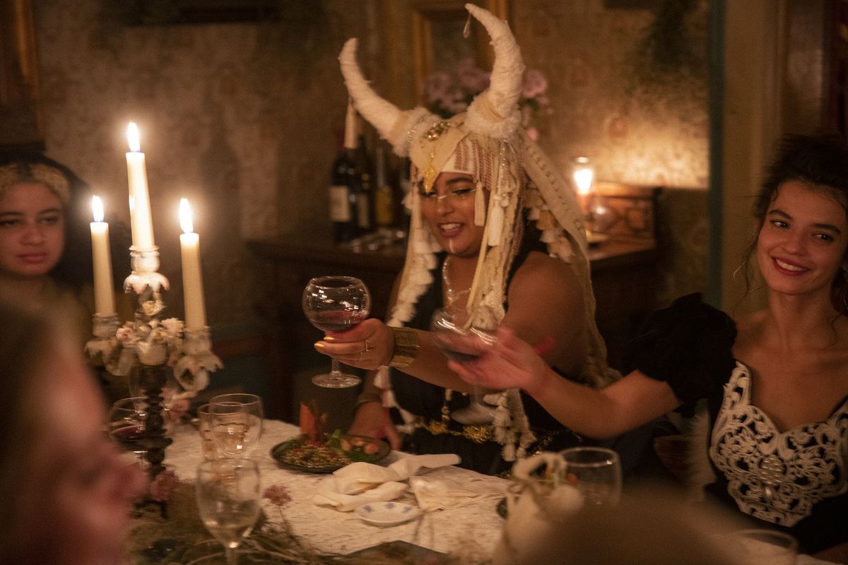 A woman in a horned headdress raises her wine glass to toast with the woman seated next to her.