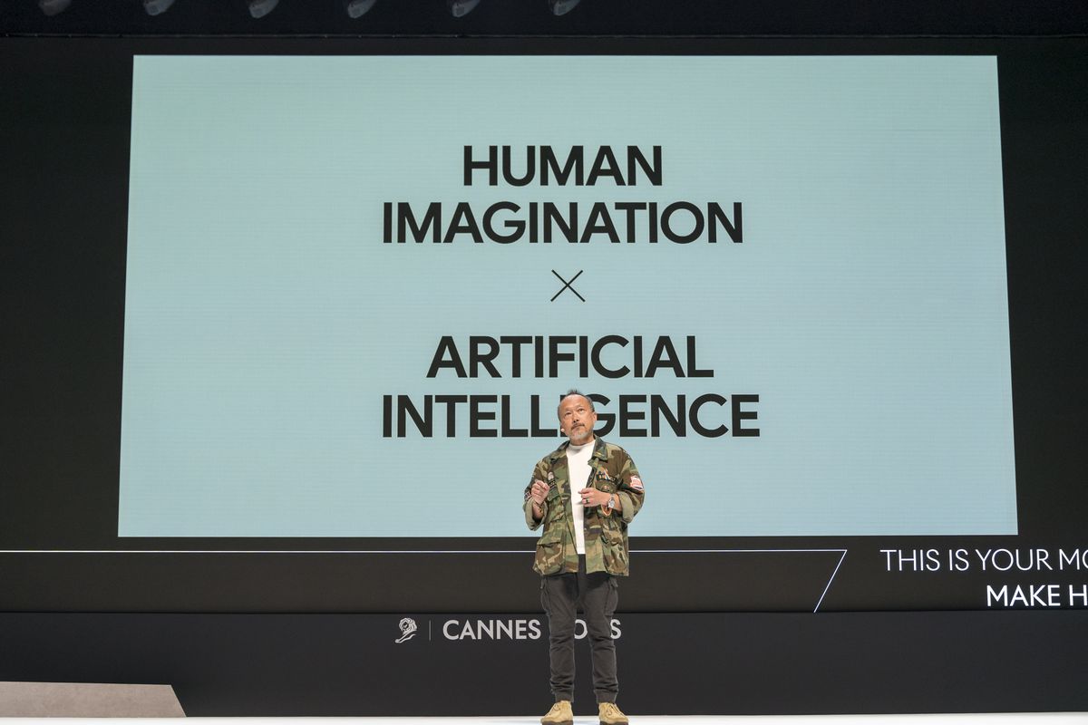 A presenter onstage in front of a screen that reads “Human intelligence x artificial intelligence.”
