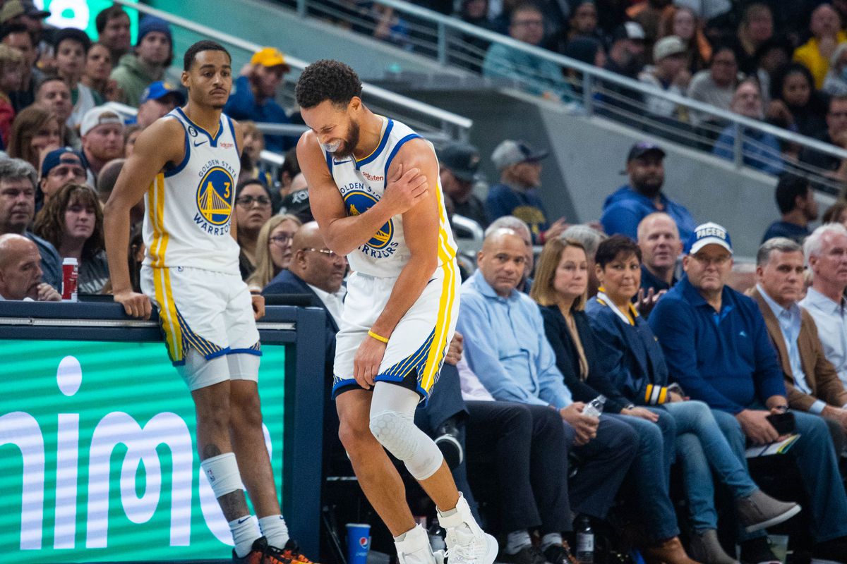 Steph Curry holds his shoulder in pain while Jordan Poole watches in the background