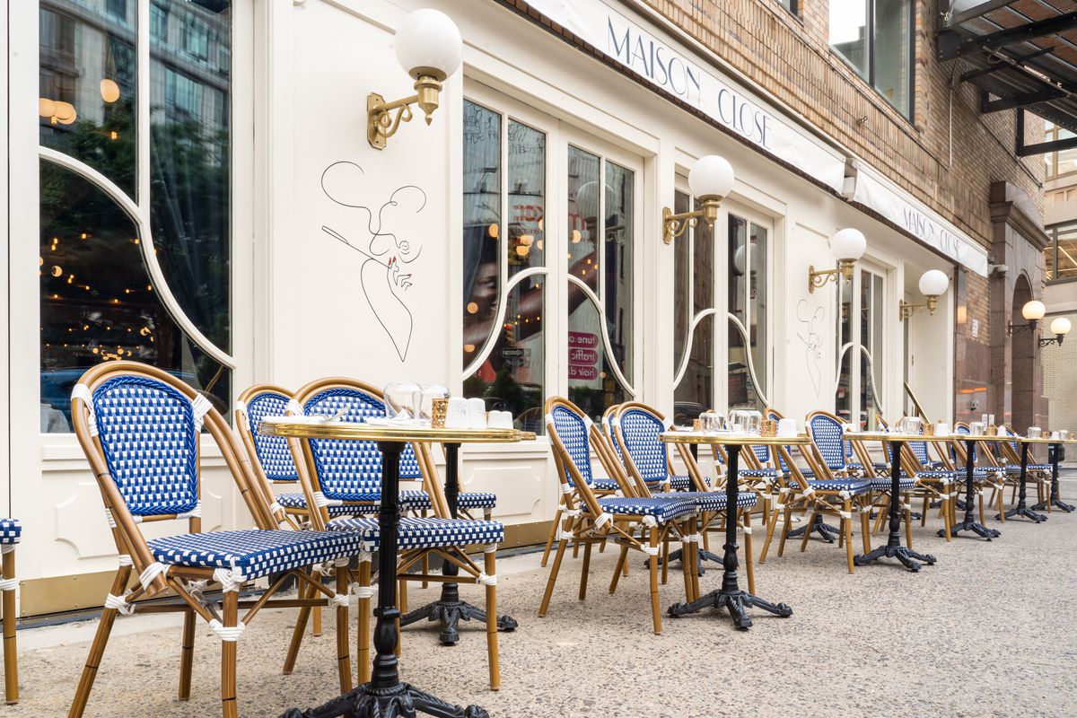 The exterior of a restaurant with sidewalk tables set up and paired with blue patterned chairs.