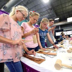 Emily Reading, Aunika Kemp and Carely Lewis try their hand at leatherwork at the Salt Lake County Fair in South Jordan on Friday, Aug. 4, 2017.
