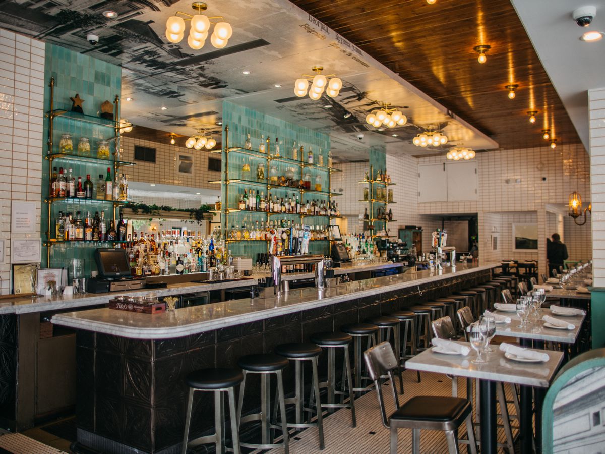 A bar with teal walls and white subway tile, with bottles on the back bar, at Ambar in Washington DC, one of the city’s best bars for a first date.
