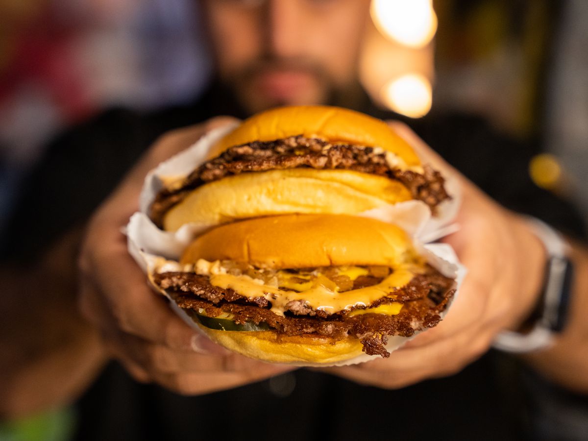 Abbas Dhanani holds up two smash burgers at Burger Bodega.