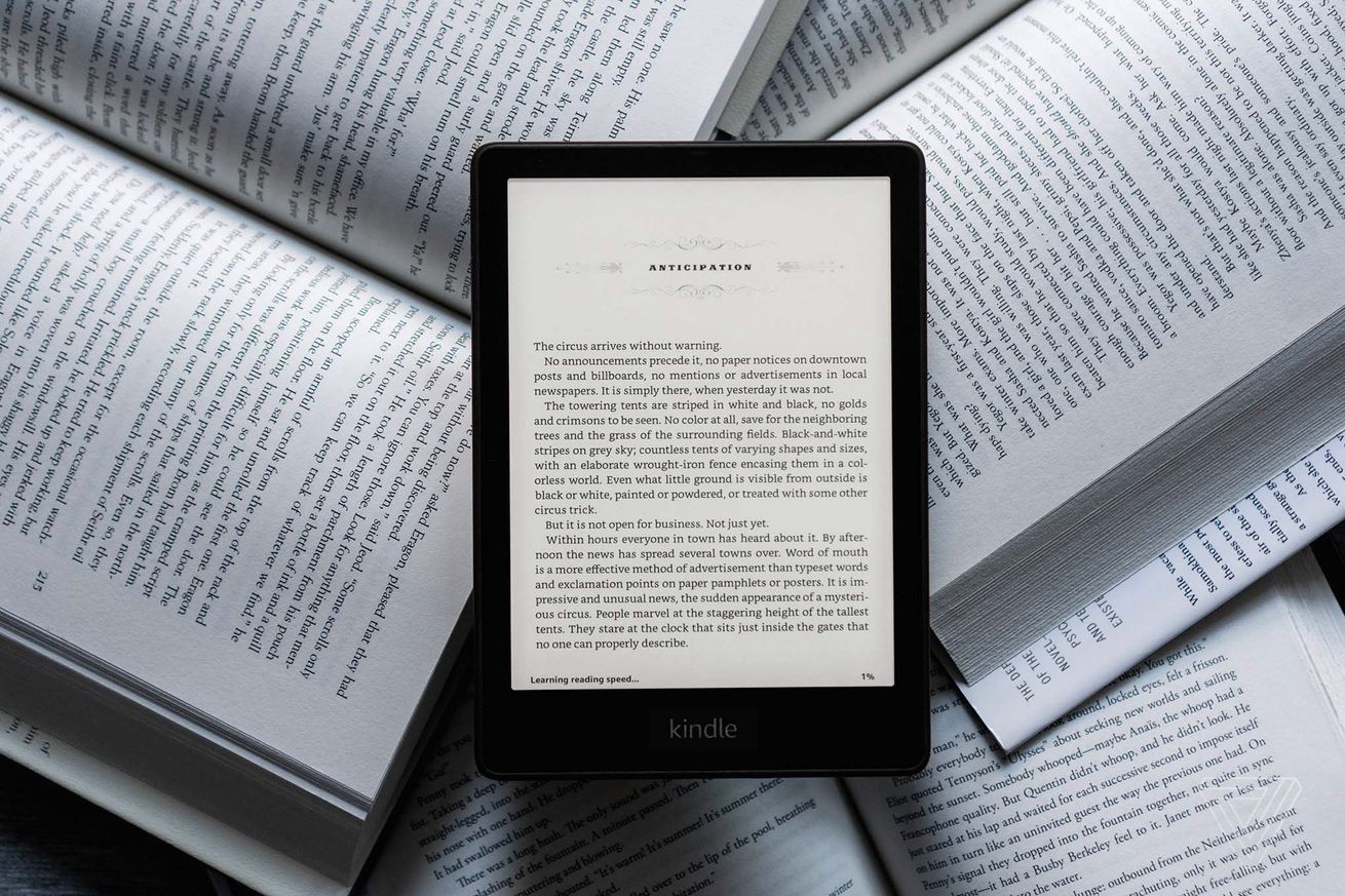 The Kindle Paperwhite lying on a bunch of physical books while turned on.