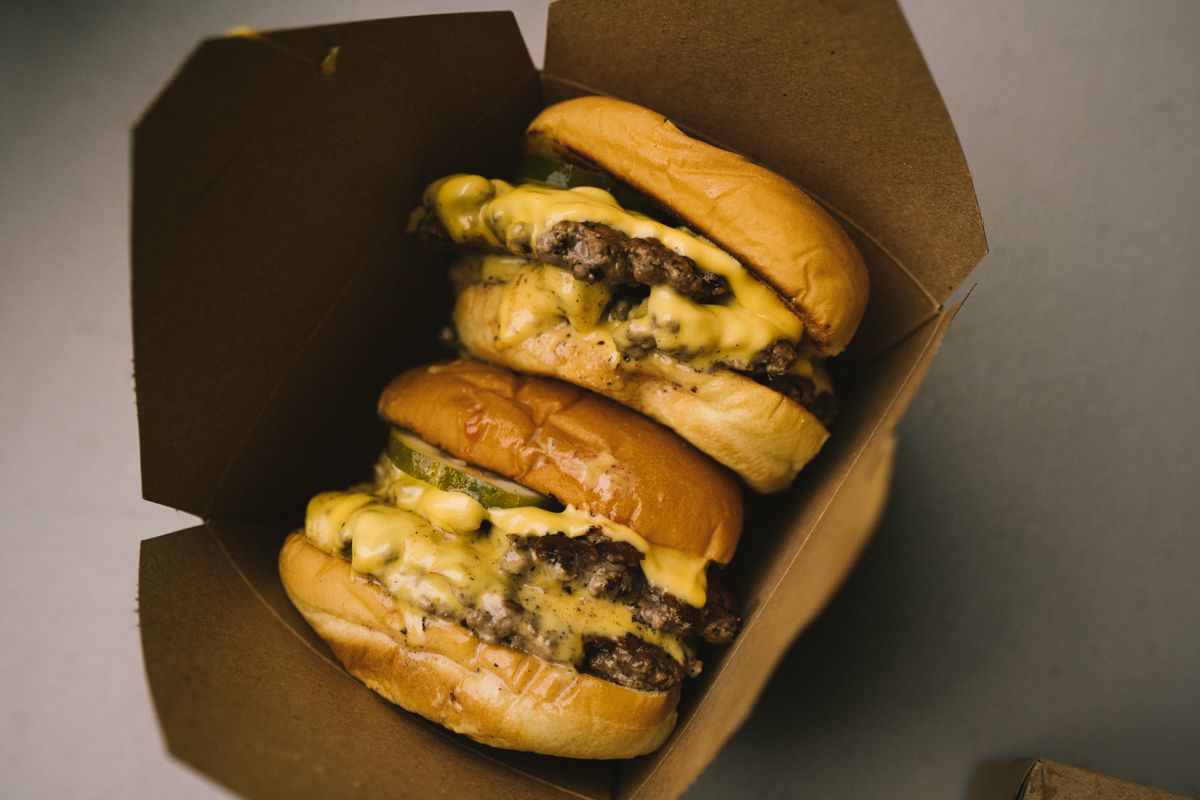 Two meat cheeseburgers placed vertically in an open brown food container