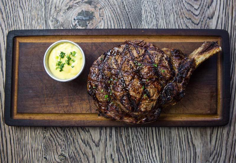 Steak on a wooden board with a pot of bearnaise sauce at Sophie’s, one of London’s best steak restaurants