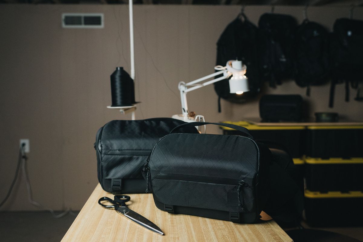 Two black Moment Rugged Camera Sling bags on a wooden table with a lamp in the background