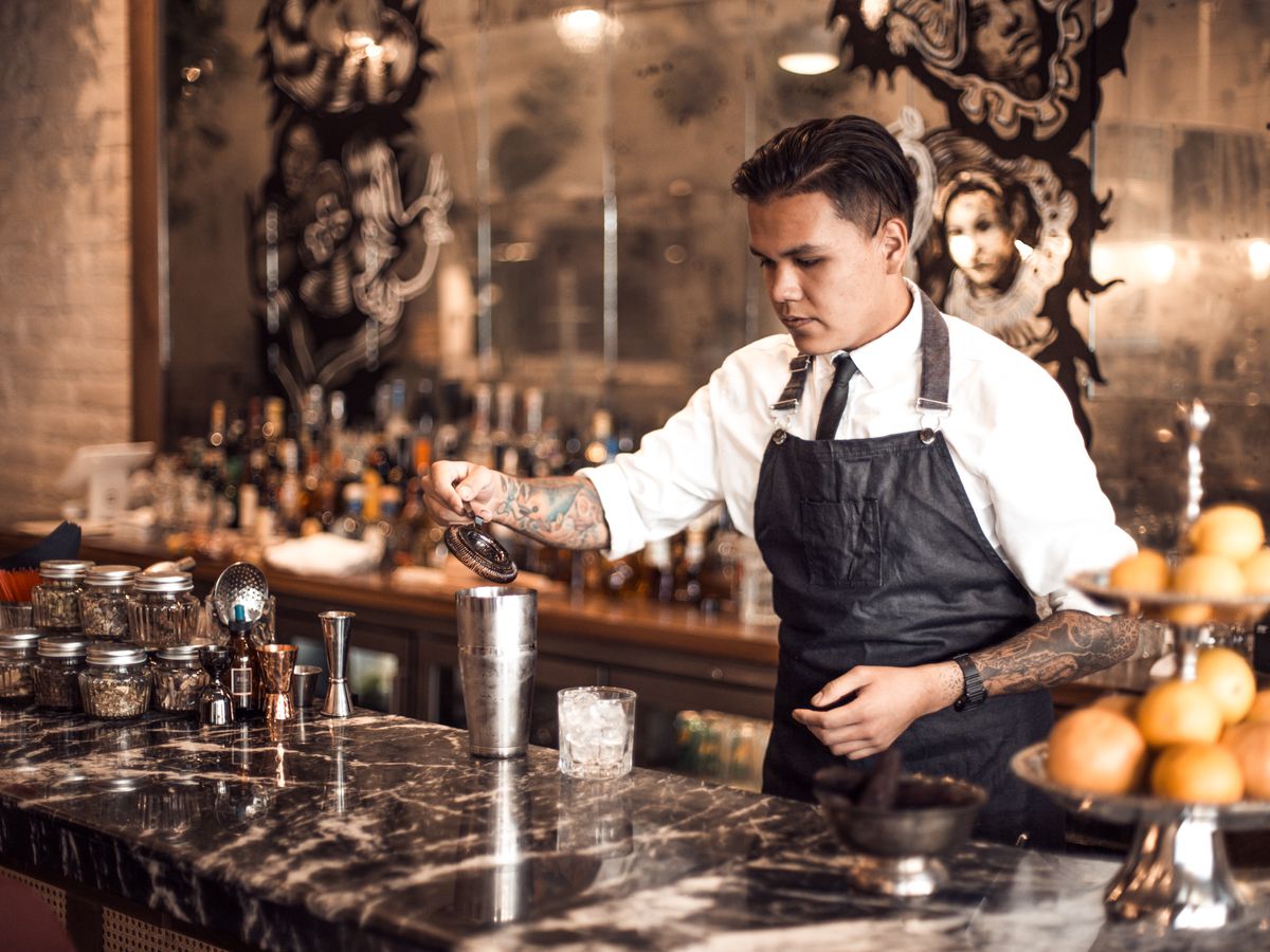A man behind a bar makes a cocktail.
