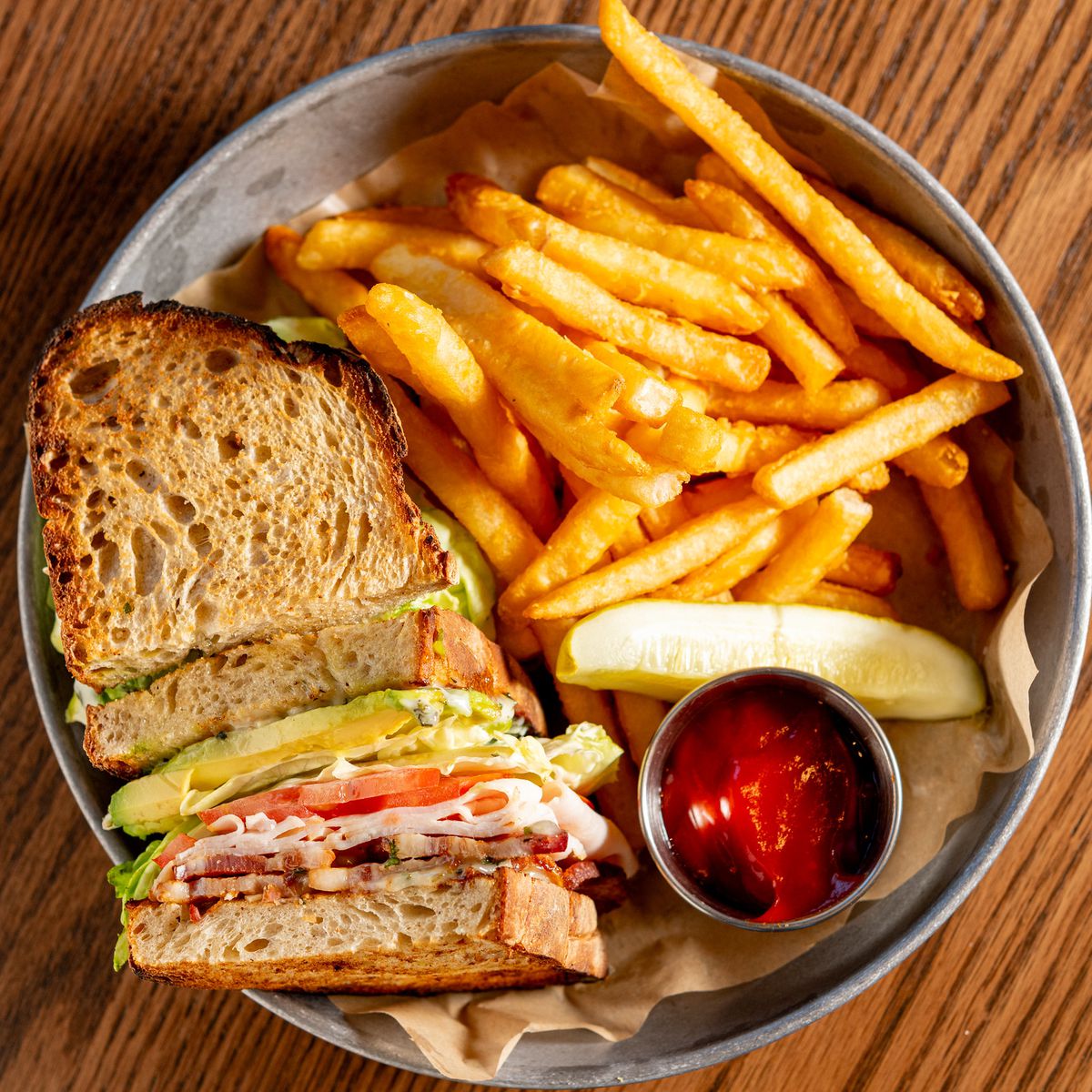 A round metal plate holds a large sandwich and French fries.