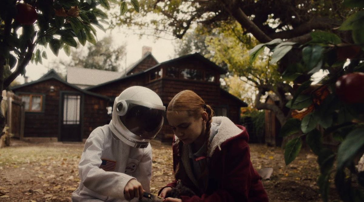 A young girl sits next to a young boy wearing an astronaut suit outside in front of a house in Spoonful of Sugar.