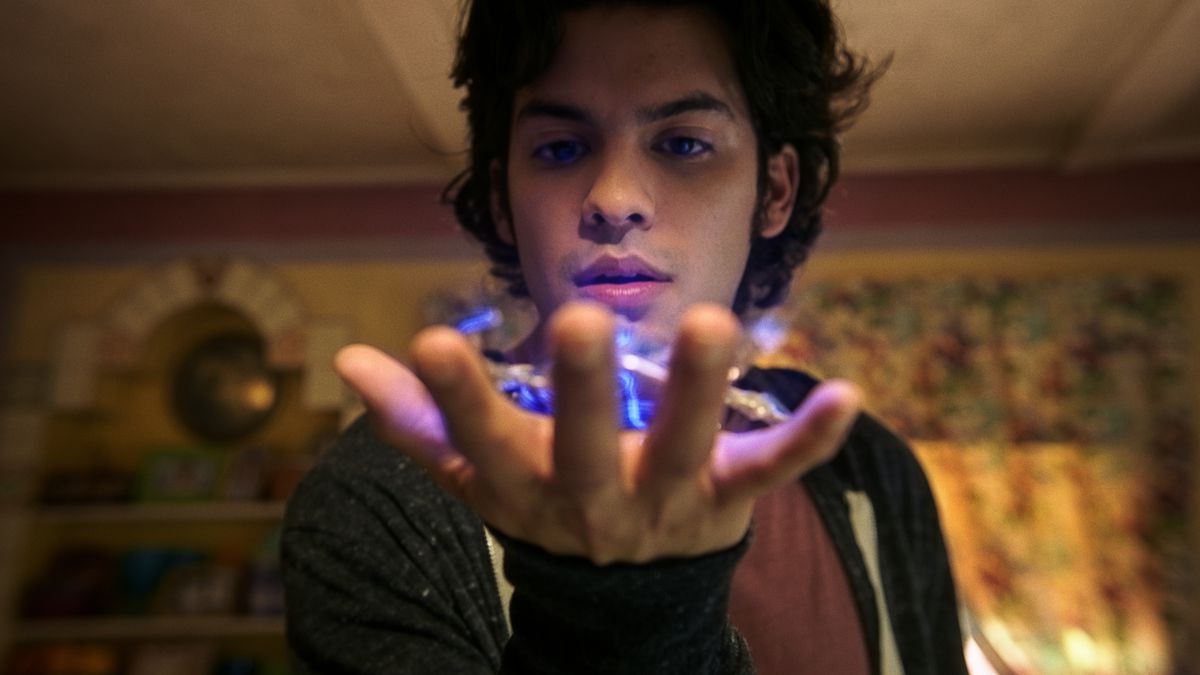 Jaime Reyes (Xolo Maridueña) holds a glowing alien scarab beetle in his palm and stares at it up close in Blue Beetle