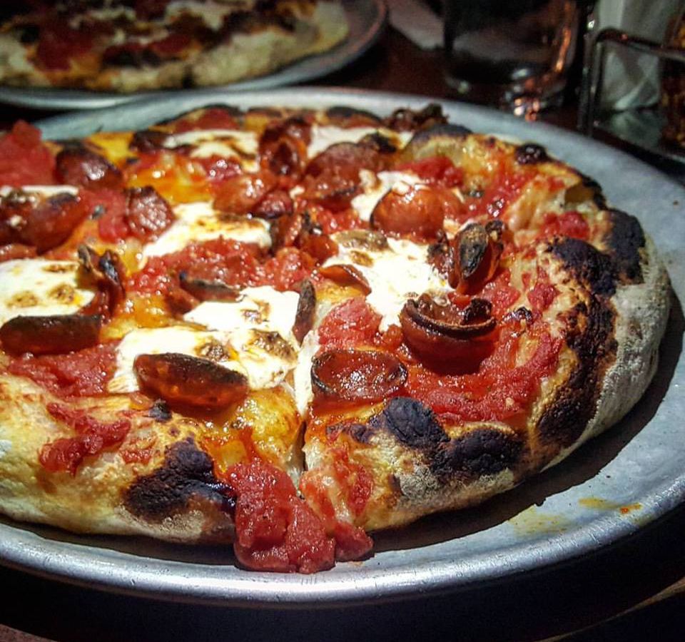 Closeup shot of a charred, thick pepperoni pizza, where the pepperoni is curled up into little cups