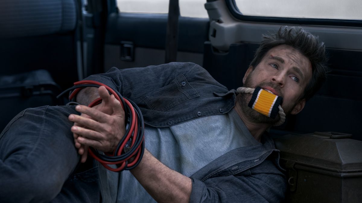 Chris Evans lies in the back of a truck, filthy and with his hands tied together with red and black wires, wearing a gag made out of a sweatband shoved into his mouth and a thick rope securing it. This is not meant to illustrate the best way to watch Ghosted, but it isn’t the worst way, either.