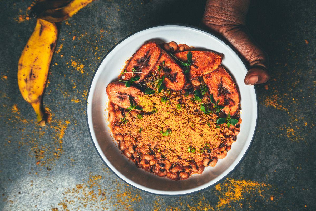 A white bowl of grains with plantains and beans is held by a hand