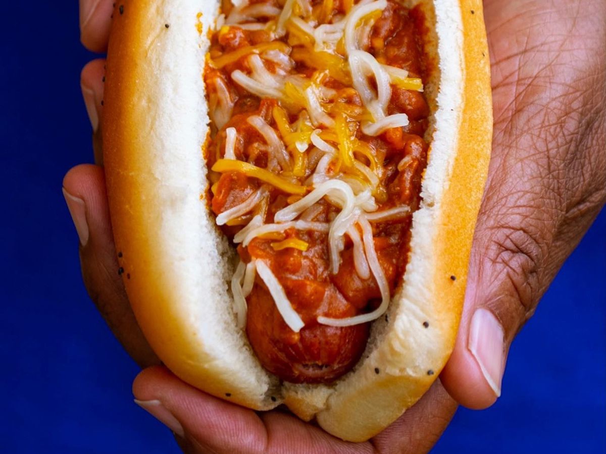 Someone holding up a hot dog in a bun with sauce and shredded cheese on it.