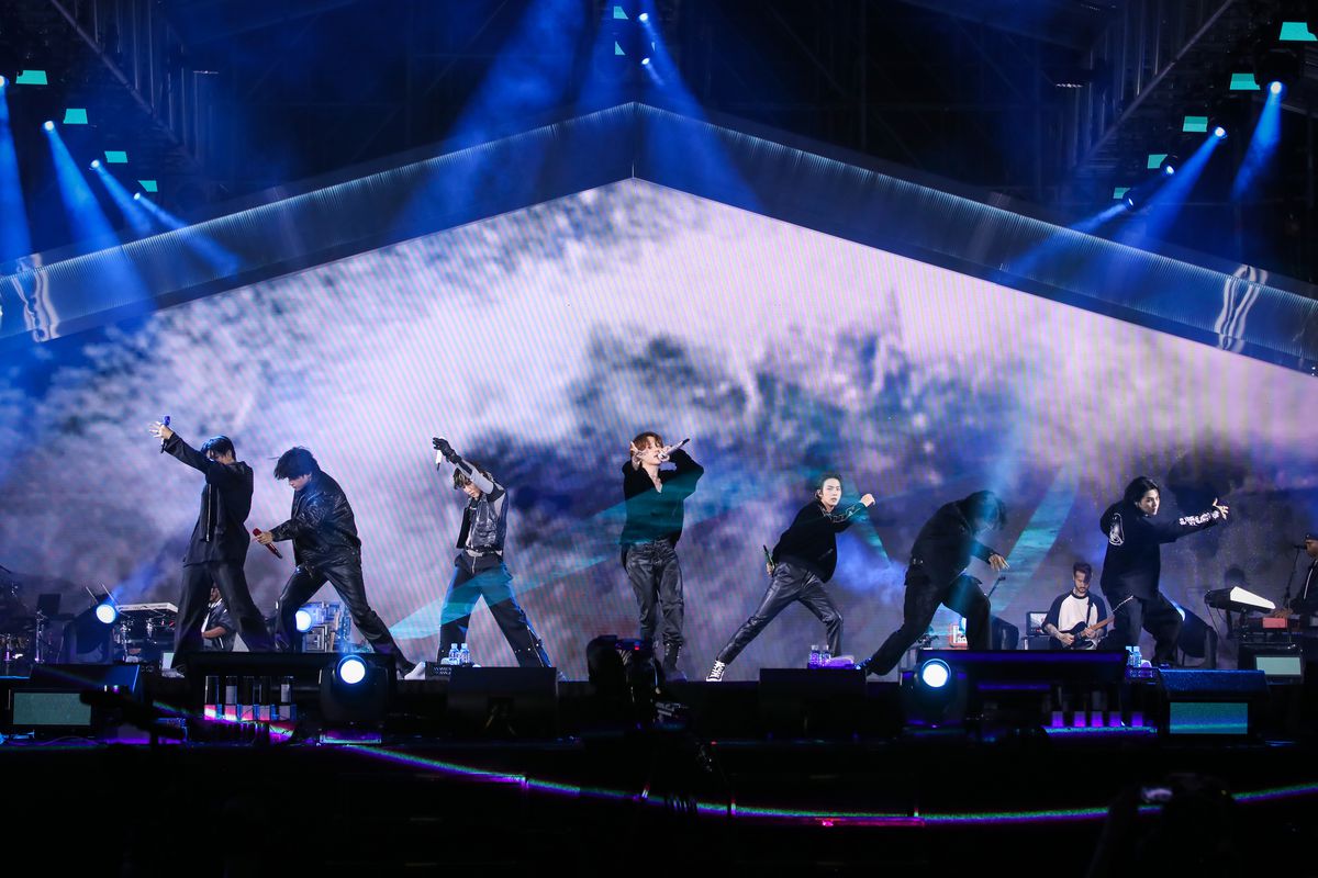 BTS strike various poses on stage, as a screen behind them displays a water spray or misty image.