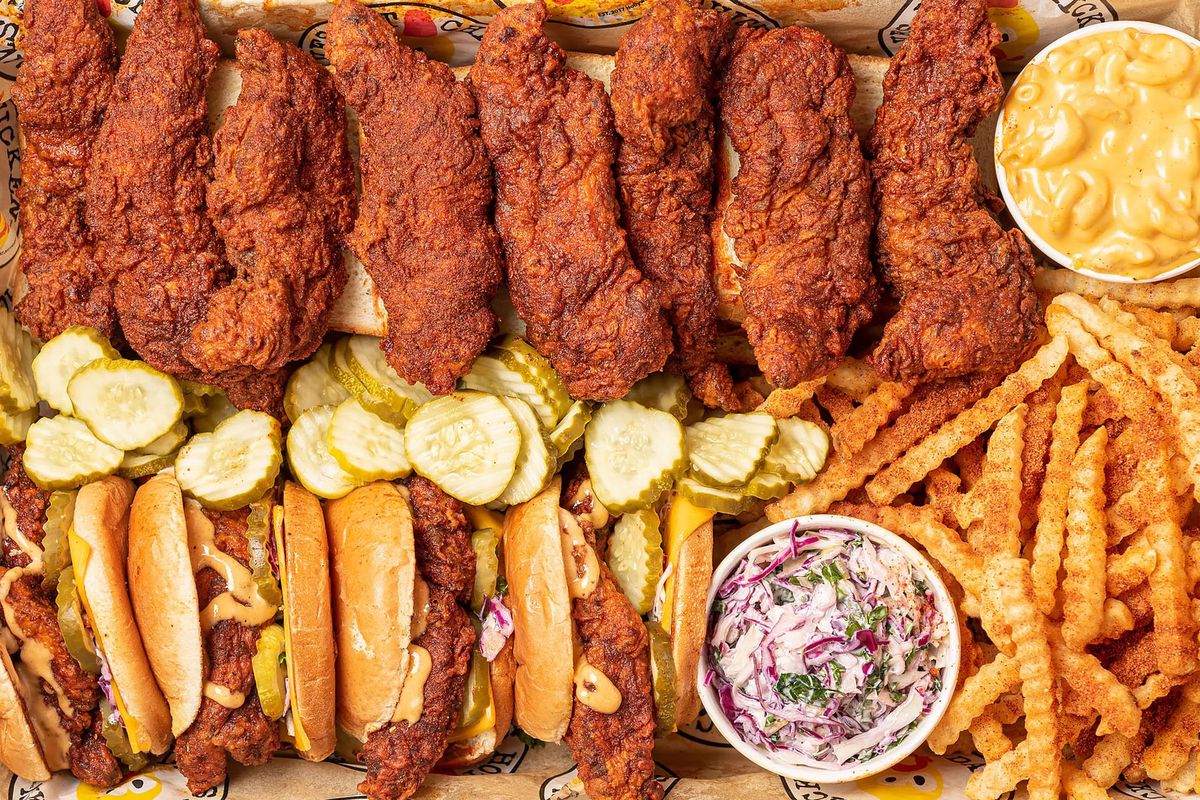 An overhead photograph of a tray overflowing with chicken tenders, sandwiches, fries, and sides.