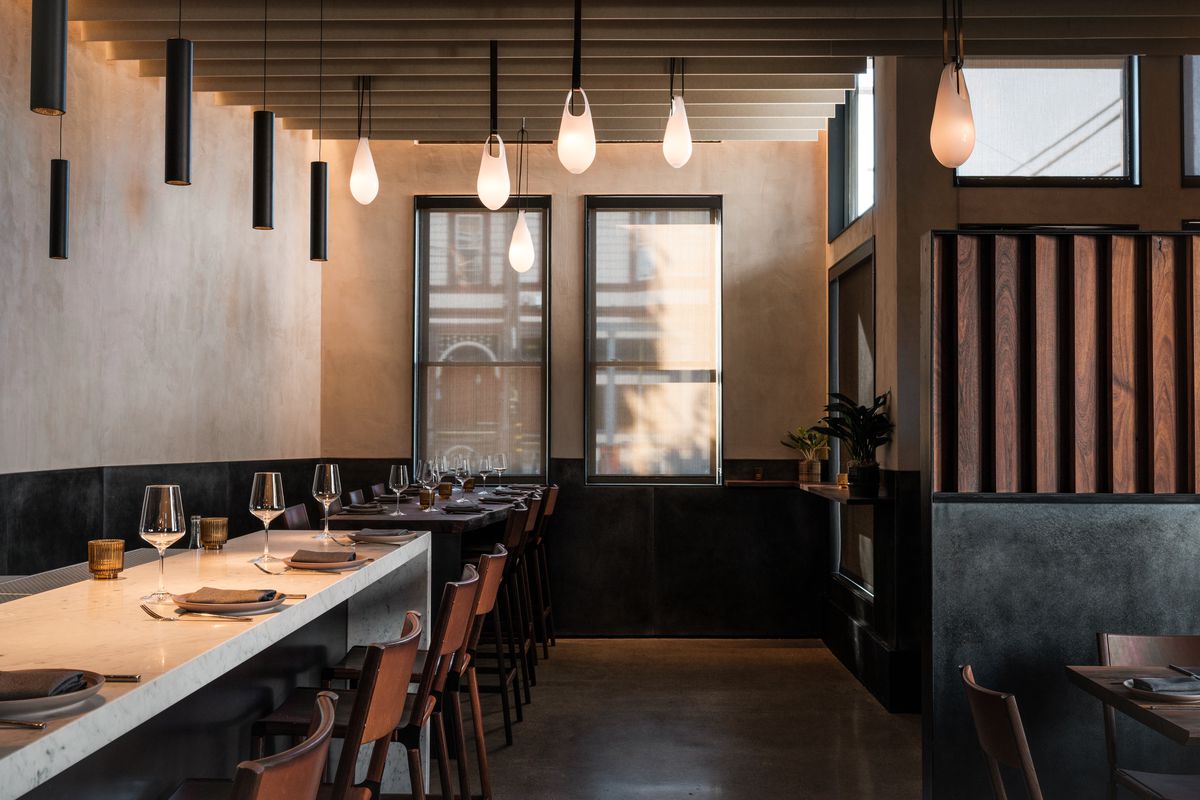 The interior of Flour + Water with white stone community tables and warm, beige colored walls.