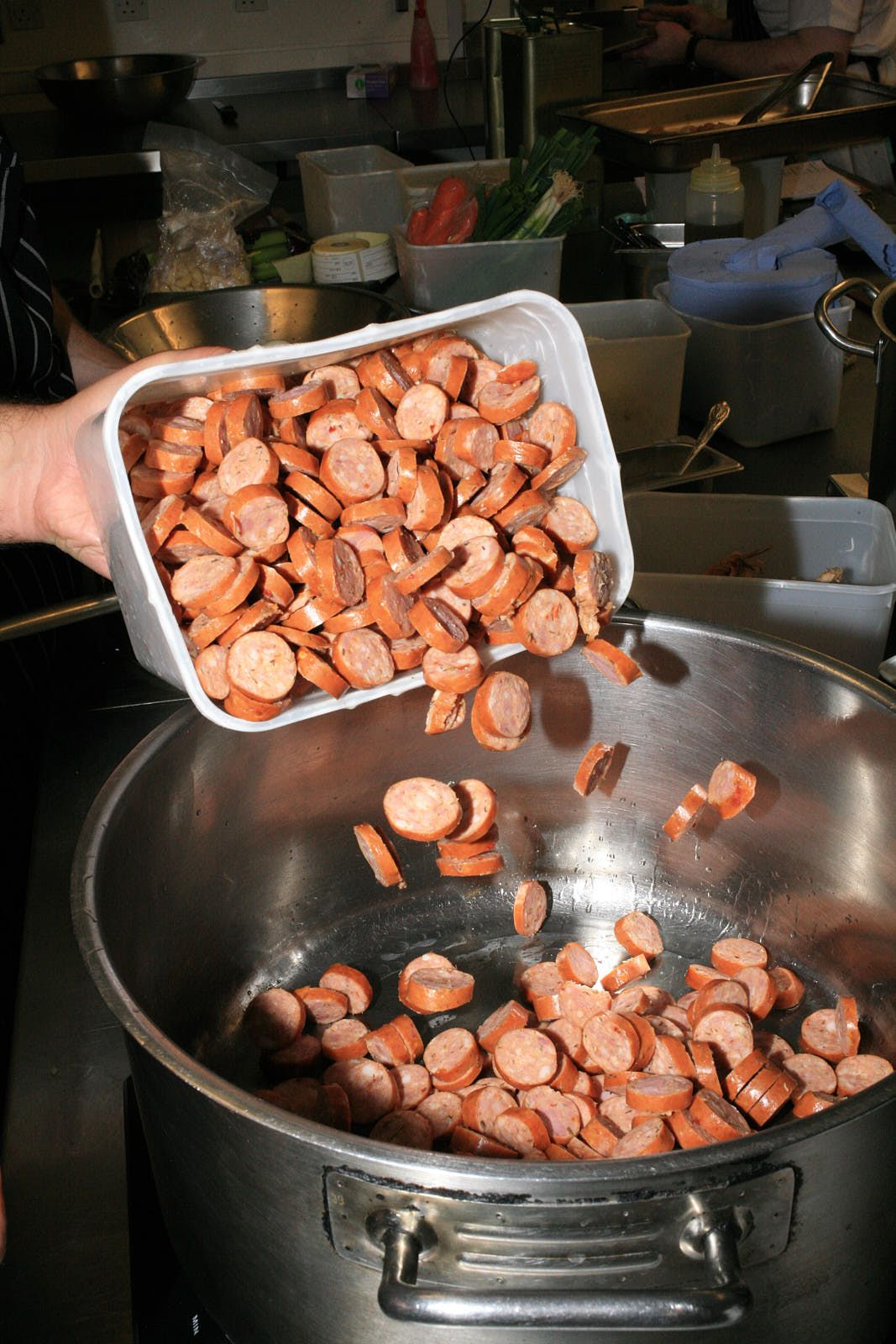 The tub of andouille is poured into a large steel pan, the coins bouncing in as it is poured from a height.