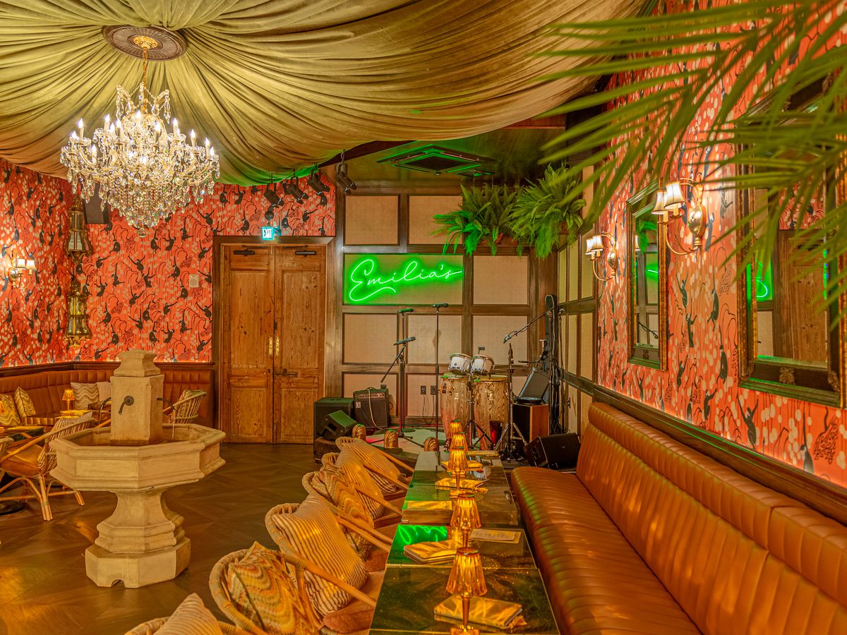 The interior of Emilia’s Havana with banquettes, a fountain, a live music stage, and a neon sign that reads “Emilia’s”.