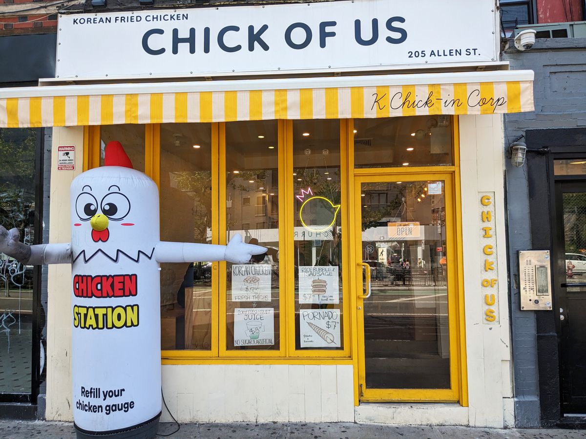 A blow up rubber chicken next to a yellow storefront.
