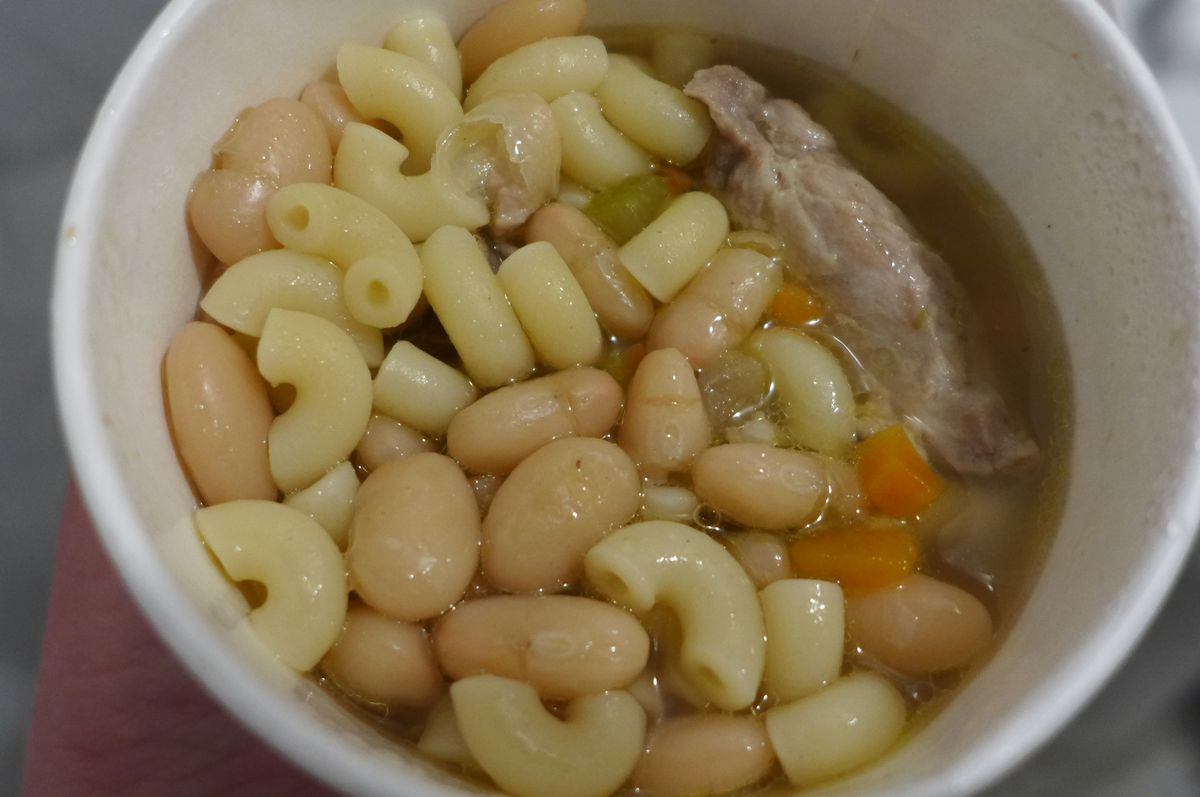 A round paper container with elbow macaroni, white beans, and pork.