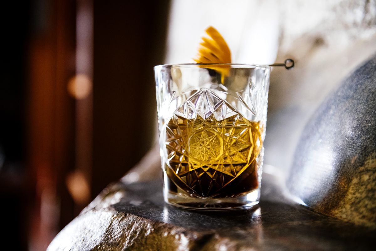 A brown cocktail in a etched glass tumbler with an orange peel garnish. 