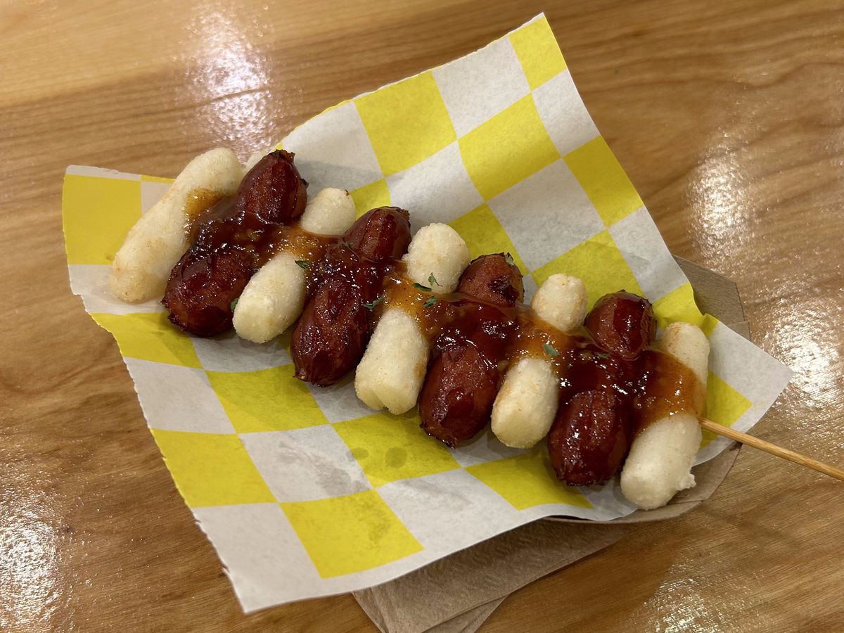 Rice cakes and charred sausages are impaled on a skewer with sauce.