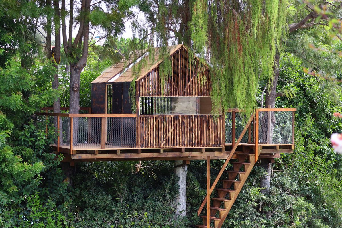 Wooden pitch-roofed treehouse in a backyard.