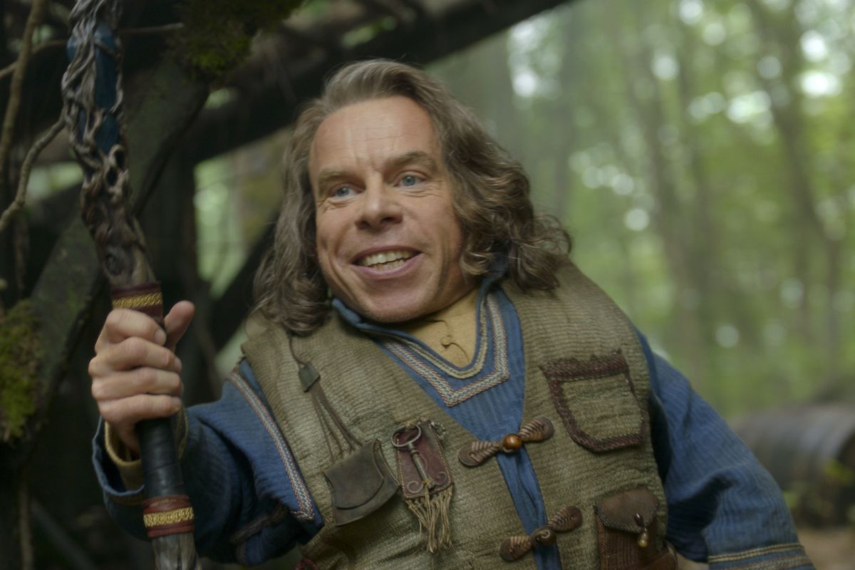 Warwick Davis grins, holding a staff, as Willow Ufgood in Willow.