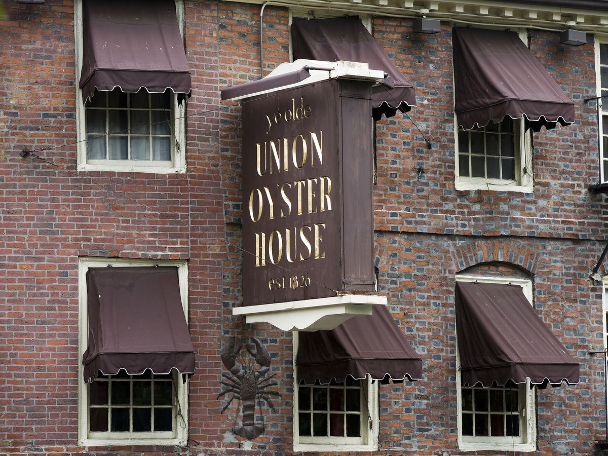  A red brick building with a sign hanging off the side that says “Union Oyster House” in faded gold lettering.